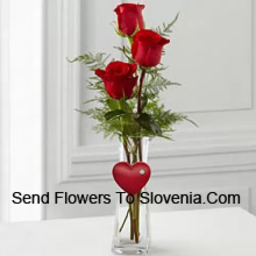 3 Red Roses In A Glass Vase Having A Small Heart Attached To It